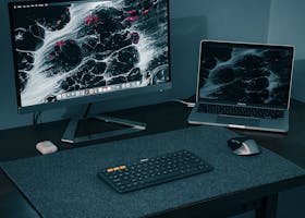 Sleek computer setup featuring monitor, laptop, keyboard, and mouse on a black desk.